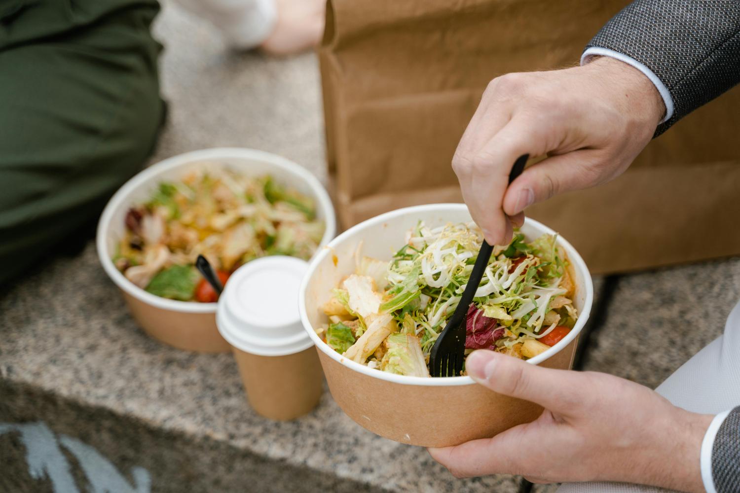 someone eating salad out of a compostable package photo: Photo by MART PRODUCTION from Pexels: https://www.pexels.com/photo/a-close-up-shot-of-a-person-eating-food-from-a-takeaway-container-8165227/