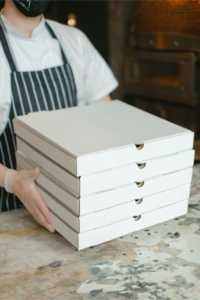 A person holding a stack of pizza boxes Photo by Anna Shvets: https://www.pexels.com/photo/person-holding-white-wooden-box-5953555/
