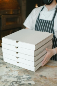 A person holding a stack of pizza boxes Photo by Anna Shvets: https://www.pexels.com/photo/person-holding-white-wooden-box-5953555/