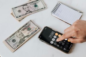 someone typing into an iphone calculator. Photo by Photo By: Kaboompics.com: https://www.pexels.com/photo/crop-unrecognizable-financier-using-calculator-on-smartphone-near-dollar-banknotes-4386324/
