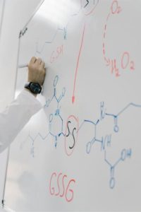 a scientist drawing chemical formulas on a whiteboard: Photo by Mikhail Nilov: https://www.pexels.com/photo/person-wearing-lab-coat-writing-formula-on-white-board-8851602/