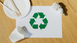 Recycling symbol surrounded by food service ware. Photo by Artem Podrez: https://www.pexels.com/photo/light-bulb-paper-cup-plate-forks-and-recycling-pictograph-6990568/