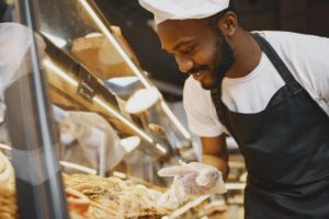 a food industry professional looking at their products. Photo by Gustavo Fring: https://www.pexels.com/photo/cook-in-an-apron-pointing-at-a-pastry-product-on-a-display-7447275/