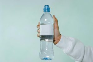 a water bottle with a blank label: Photo by MART PRODUCTION: https://www.pexels.com/photo/person-holding-clear-plastic-bottle-8217303/ 