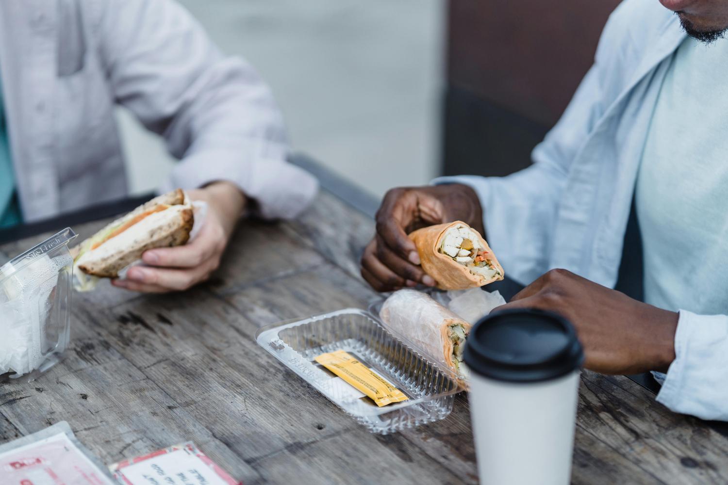 people eating sandwiches on the go. Photo by Mizuno K: https://www.pexels.com/photo/close-up-of-two-men-eating-lunch-13335060/
